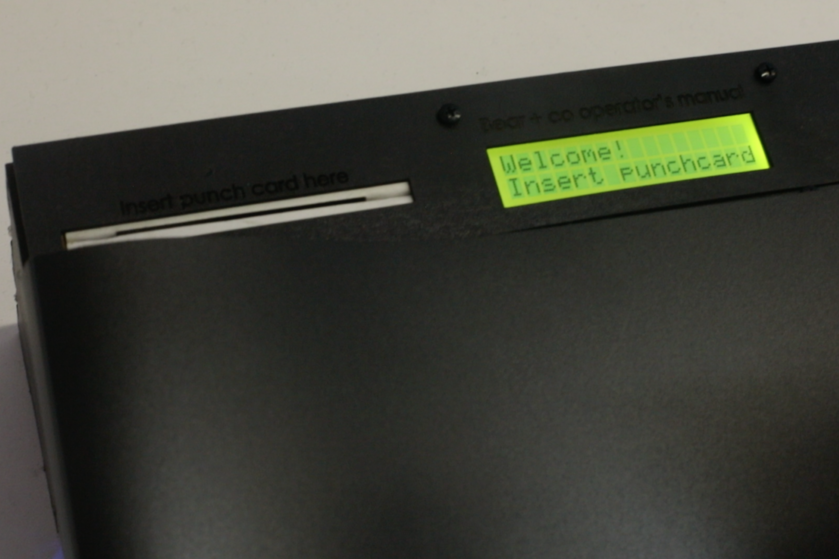 Close-up of the station’s LCD screen prompting “Welcome! Insert Punchcard,” guiding participants through the sign-in interaction.