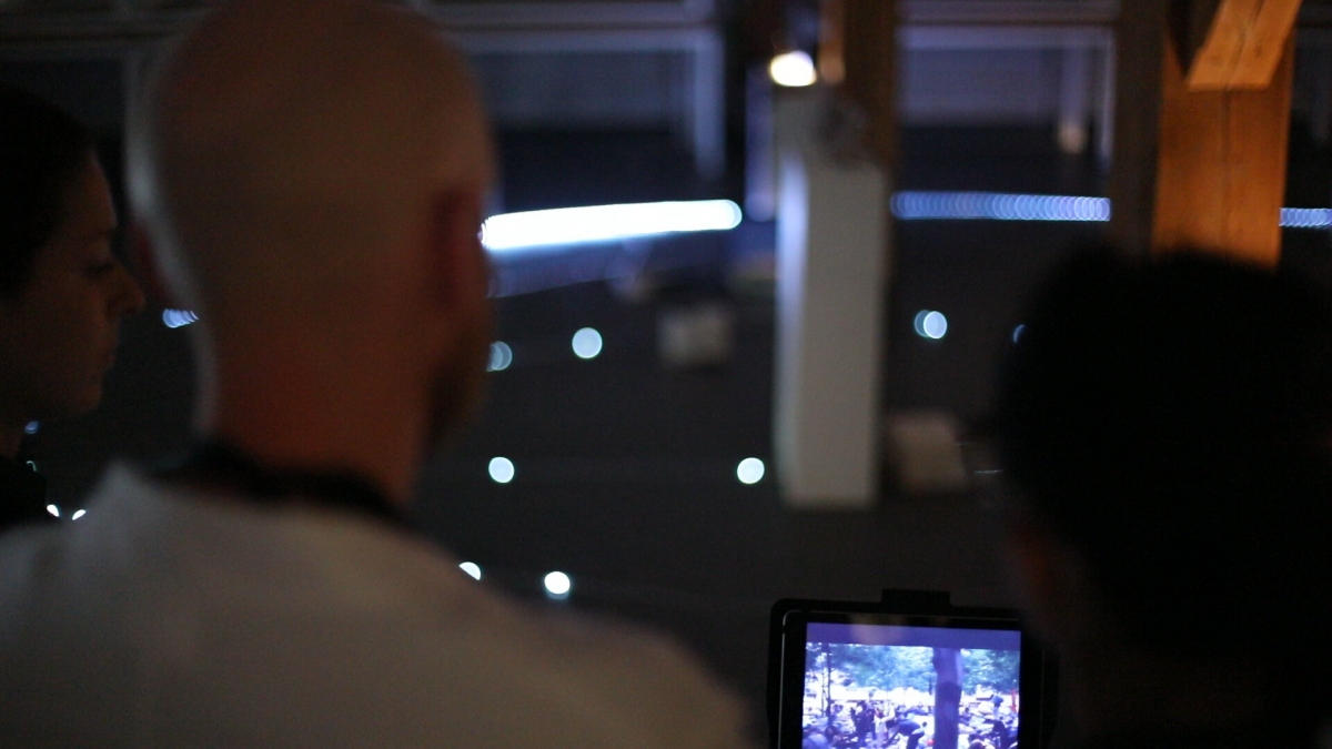 Participants gather around a dimly lit loop of LED markers in the exhibition hall, peering at a tablet that streams real-time projections of future energy scenarios—evoking the immersive, game-like environment of Escaping the Strange Loop.